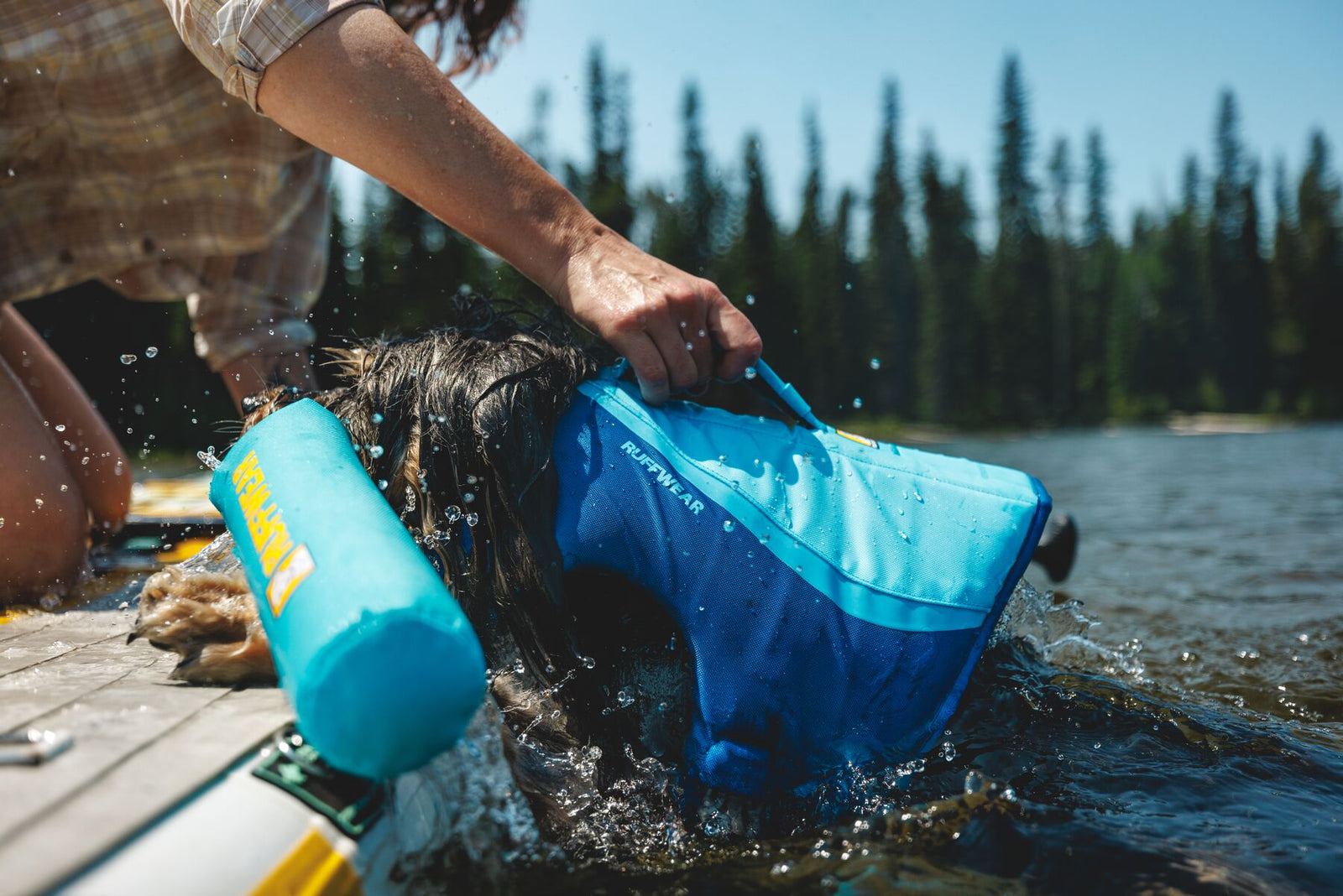 Person lifting a wet dog out of a lake using the handle on the Ruffwear Float Coat in Deep Blue, from a dock.