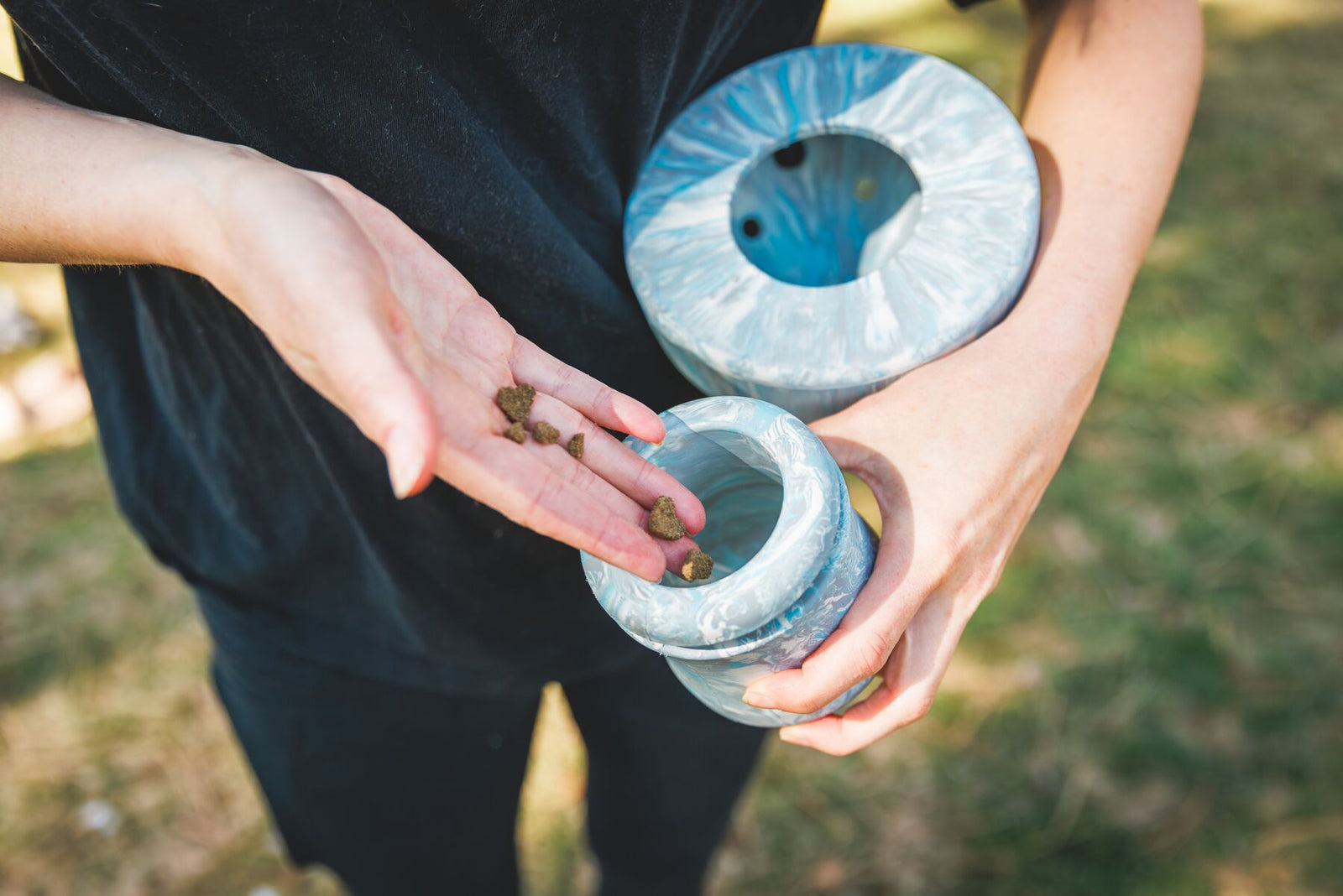 Owner's hands loading kibble into the stem of the Ruffwear Porcini enrichment toy in Gray Sky with the cap held separately, grass background