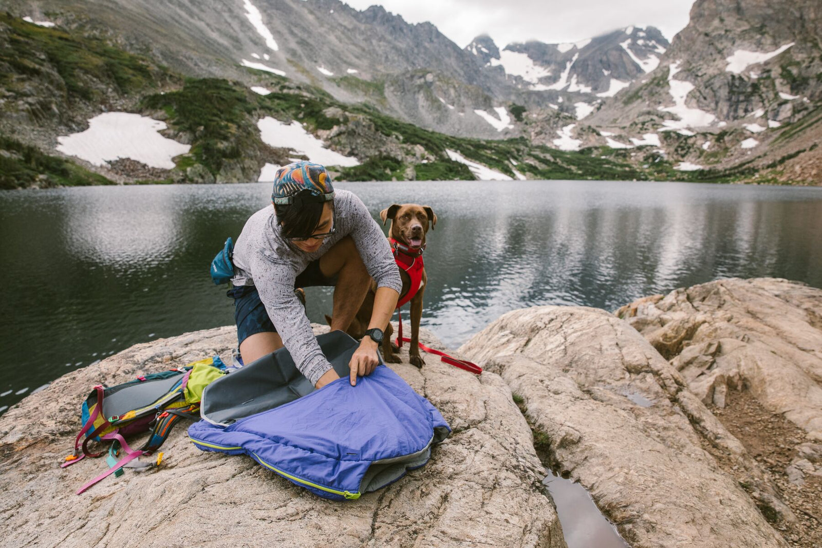 Person laying out Ruffwear Highlands Pad on rocky ground beside a mountain lake
